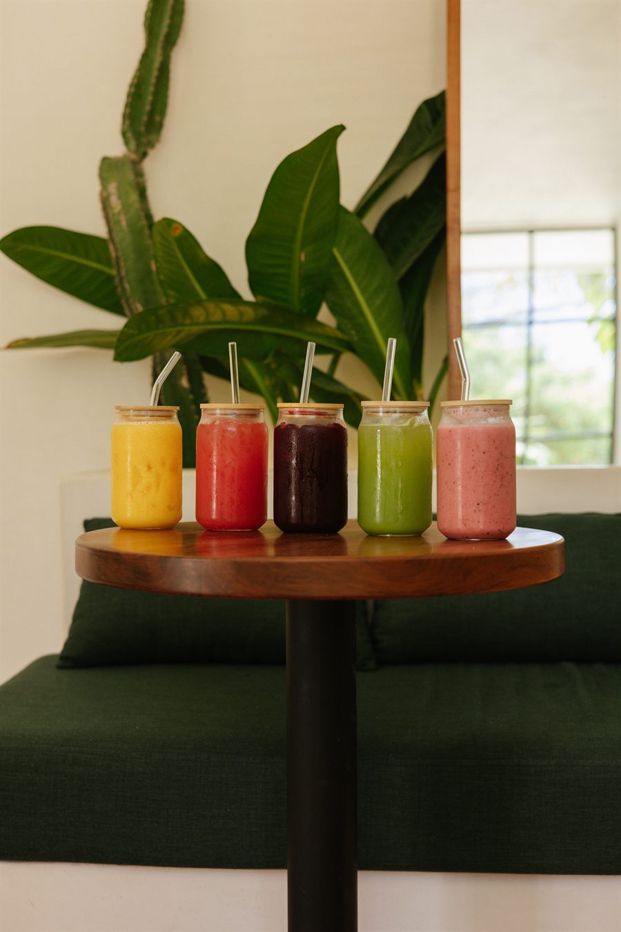 Five colorful juices and smoothies on a wooden table at OLIVO